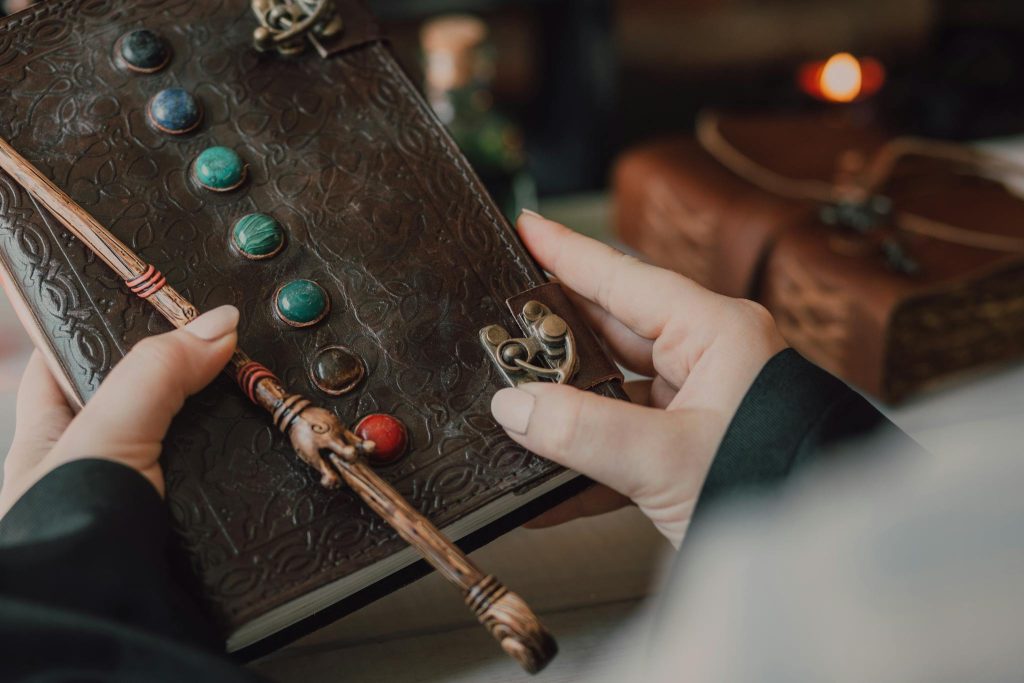 Hands holding a decorative journal and wand, evoking a magical and mystical theme.